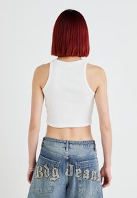 Hvit croppet tanktopp med ribbet tekstur, kombinert med blå denimjeans med brodert "Bdg Jeans" bak.