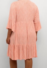 Robe à imprimé floral en tissu léger et doux. Présente des manches courtes en forme de cloche, un ourlet à volants superposés et une coupe décontractée en corail et blanc.