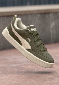 Green suede sneakers with white accents, featuring a padded collar, lace-up design, and a thick cream-colored sole.