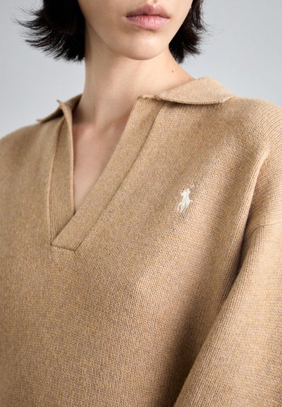 Beige gebreid trui met een V-hals en kraag. Voorzien van een klein wit logo op de linkerborst, met een gestructureerde afwerking.