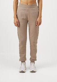 Beige joggings med en tapered ben, elastisk talje og sidestriber med et subtilt mønster. Lavet af blødt, struktureret stof.