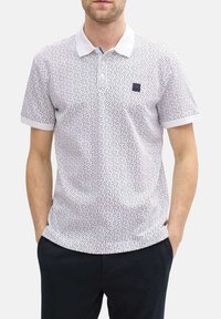 Polo shirt à manches courtes en blanc avec un motif noir éparpillé, arborant un col contrasté et un petit logo sur la poitrine.
