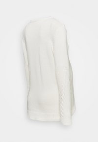 Valkoinen neulepaita, jossa on kaapelikudottu kuviointi hihoissa ja ribbireunus. Kangas näyttää pehmeältä ja siinä on rento istuvuus.