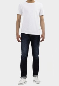 Camiseta blanca de manga corta, jeans oscuros ajustados con puños enrollados y zapatillas blancas con detalles en negro. Conjunto simple y casual.