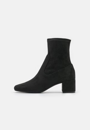 Black suede ankle boot with a rounded toe, mid-height block heel, and smooth upper extending above the ankle.