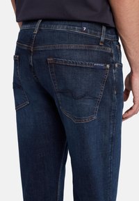 Jeans in denim blu scuro con vestibilità dritta, dotati di due tasche posteriori, dettagli di cucitura sottili e un'etichetta logo in vita.