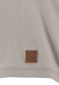 Tela beige con un dobladillo cosido y un pequeño parche de cuero marrón etiquetado "KEY LARGO" que presenta un logotipo en relieve.