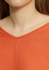 Oranje gebreide top met een V-hals, voorzien van een gladde textuur en subtiele stiksels langs de halslijn.