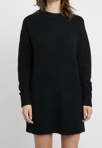 Abito in lana nera con collo alto, maniche lunghe e polsini a coste, caratterizzato da una vestibilità morbida e un tessuto soffice e texture.