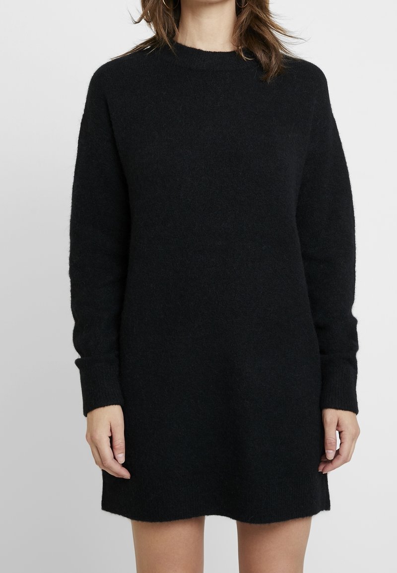 Abito in lana nera con collo alto, maniche lunghe e polsini a coste, caratterizzato da una vestibilità morbida e un tessuto soffice e texture.