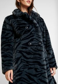 Manteau en fausse fourrure avec un motif à rayures de tigre bleu foncé et noir, croisé, grand col et boutons noirs. Texture douce.