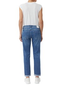 Niebieskie dżinsy z prostą nogawką, podwiniętymi mankietami i dwoma tylnymi kieszeniami, zestawione z dopasowanym białym topem bez rękawów.