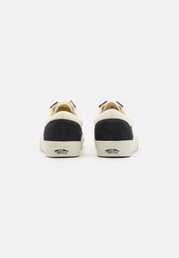 Et par lave Vans sneakers i sort og hvidt vist fra bagsiden, der viser "Off The Wall" logoet på hælen.
