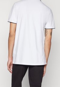 Vit polo skjorta med svart detalj på ärmarna. Korta ärmar, krage och rak nederkant. Slät textur, bärs med mörka byxor.