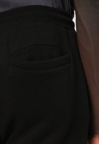 Calças de jogging pretas com um tecido texturizado, apresentando uma cintura elástica suave e um detalhe discreto de bolso lateral.