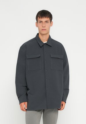 Dark gray overshirt made of lightweight fabric, featuring a button-up front, two chest pockets, and relaxed fit with long sleeves.
