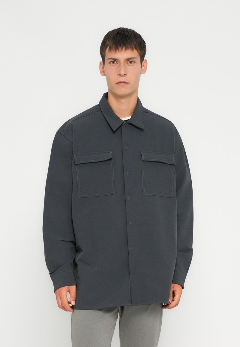 Dunkelgraues Overshirt aus leichtem Stoff, mit Knopfverschluss vorne, zwei Brusttaschen und lockerer Passform mit langen Ärmeln.
