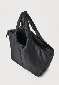 Sac fourre-tout matelassé noir avec deux poignées et une fermeture éclair supérieure, montré partiellement ouvert sur un fond clair.