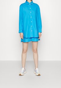 Light blue button-up shirt with a collar, paired with matching shorts. Footwear features pastel accents and a textured sole.