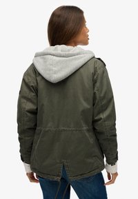 Olijfgroene utiliteitsjas met grijze capuchon, elastische manchetten, taillekoord en een geventileerd rugdetail, gemaakt van een katoenmix stof.