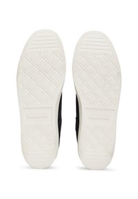 Mustat kangastennarit valkoisilla kumipohjilla. Pohjassa on timanttikuvio, joka parantaa pitoa. Tavaramerkin logo on kohopainettu toiseen sivuun.