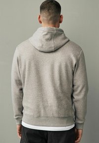 Sudadera gris hecha de una tela suave, con capucha ajustable, puños y dobladillo acanalados, con un corte relajado y detalles mínimos.