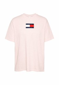 Camiseta de algodón de color rosa claro con manga corta y cuello redondo, que presenta un diseño de logo rectangular en azul marino, blanco y rojo en el pecho.