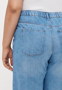 Light blue denim pants with an elastic waistband, featuring two back pockets and a straight-leg cut. Texture is soft with a slight stretch.