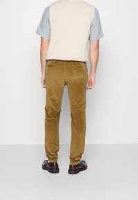 Bruine corduroy broek met een slanke pasvorm, voorzien van achterzakken en een zachte textuur, gecombineerd met een lichtgrijs T-shirt met korte mouwen en bruine schoenen.
