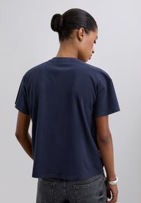 Camiseta de manga corta azul marino con un corte relajado, cuello redondo y textura de algodón suave, vista desde atrás.