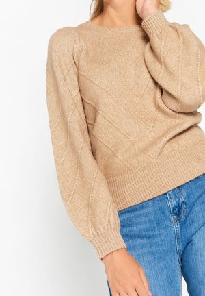 Maglione beige lavorato a maglia con un motivo a rombi in rilievo, scollatura rotonda e maniche a sbuffo, abbinato a jeans blu.