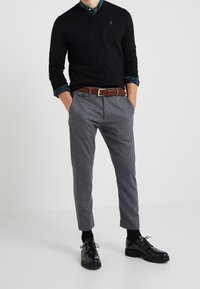 Black v-neck sweater over a green and blue checkered shirt, gray tapered trousers, brown braided belt, and black lace-up shoes.