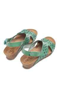 Sandalias verdes de cuero con patrones recortados, correa trasera ajustable, suela de corcho y plantilla texturada. Hechas en España.