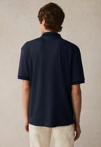 Marinblå polo t-shirt med mjuk textur, korta ärmar och en klassisk krage. Detaljer inkluderar kontrastfärger på kragen och ärmarna.