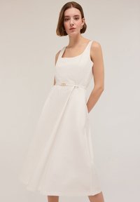 Rochie albă fără mâneci, cu decolteu pătrat, talie fixată cu un accesoriu din metal auriu și fustă în evazé. Textură din bumbac.
