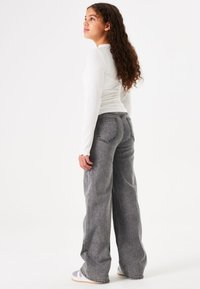 Grijze wijde jeans van textuurstof met contrasterende stiksels, gecombineerd met een aansluitend wit langemouwen shirt.