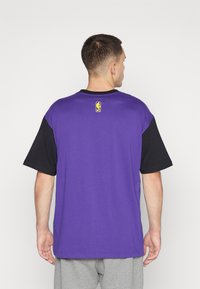Cămașă scurtă cu mânecă, purple și neagră, făcută din bumbac. Prezintă un logo pe gulerul din spate. Croială dreaptă cu o potrivire lejeră.