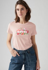 Rosa bomulls-t-shirt med blommönster och texten "Levi's" i vitt, tillsammans med högmidjade blå denimjeans.