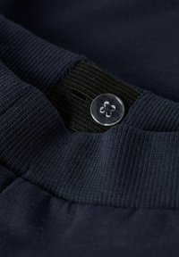 Granatowa tkanina o prążkowanej teksturze i gładkim pasie. Zawiera przezroczysty guzik z kwiatowym wzorem. Zbliżenie na szczegóły.