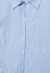 Cămașă cu dungi verticale albastre și albe, cu nasturi și guler, trei nasturi vizibili, materialul ușor încrețit.