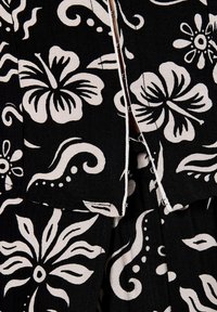 Tessuto nero con motivi floreali e swirl bianchi; presenta una chiusura parzialmente aperta e una superficie texture.