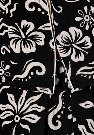 Black fabric with white floral and swirling patterns; features a partially unzipped closure and textured surface.