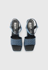 Blå denim högklackade sandaler har en fyrkantig tå, en ankelrem och en texturerad ovandel med ett upprepande mönster. Svart sula och foder.