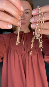 Joyería en tono dorado que presenta una cadena texturizada con elementos colgantes y una pulsera de múltiples eslabones con acentos de piedras, ambas sostenidas en manos.