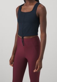 Marinblå, kort tanktopp med rutig halsringning, med en dragkedja framtill och snörningsdetalj. Kombinerad med vinröda, åtsittande leggings.