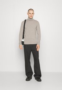 Lichtgrijze coltrui gecombineerd met losse zwarte broek; model draagt een kleine zwart-wit schoudertas en heeft zwarte schoenen aan.