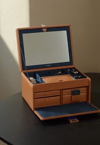 Caja de joyería de cuero marrón con forro de ante azul marino. Cuenta con un espejo, múltiples compartimentos, cajones y una bandeja deslizante para accesorios.