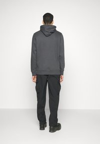 Mörkgrå hoodie med dragsnodd och ribbade ärmmuddar, tillsammans med svarta cargobyxor med sidofickor och avslappnad passform.