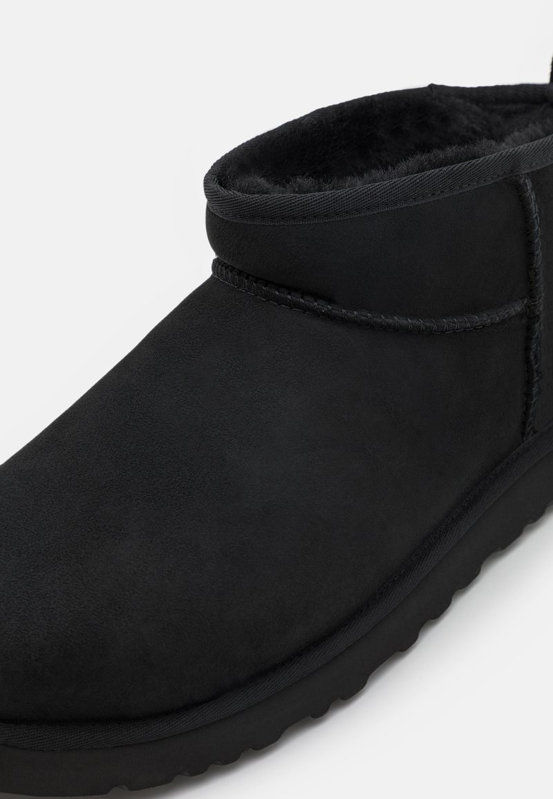 Bottine noire en daim souple avec une doublure synthétique, dotée d'une semelle texturée, de détails cousus et d'un design à bout rond.