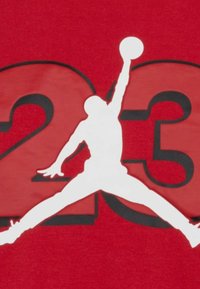 Maglietta in cotone rossa con una silhouette bianca di una figura che salta e il numero "23" in nero dietro di essa.